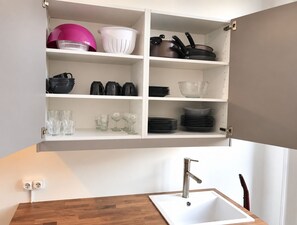 Eine Küche mit einer eingebauten Schranke, die diverses Küchengeschirr enthält, einem Spülbecken mit modernem Wasserhahn und einer Holzarbeitsplatte.