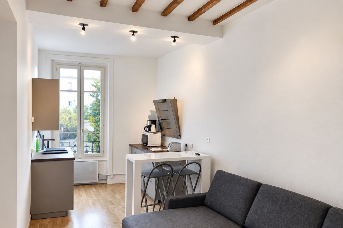Ein stilvoller Wohnraum mit Sofa, Esstisch mit Stühlen, Küchenzeile und einem großen Fenster für natürliches Licht.