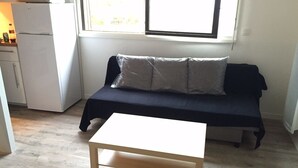 A small, compact room with a kitchenette, a dark blue sofa with cushions, and a white table in the center. - Apartment standing Cap Ferret center (Cap ferret)