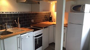 A compact kitchen with white cabinetry, a black tiled backsplash, a built-in microwave, and a dishwasher. - Apartment standing Cap Ferret center (Cap ferret)
