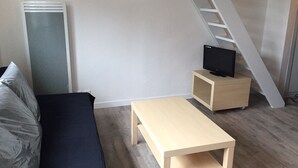 A compact living space with a sofa, a small wooden table, a TV on a stand, and a staircase. - Apartment standing Cap Ferret center (Cap ferret)