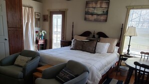 A bedroom with a large bed, two armchairs, a small table, and a window with blinds. - Little lake house/ Fish cabin get away (Chandler)