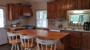 A kitchen with wooden cabinets, a central island with chairs, a stove, a window with blinds, and a coffee maker. - Little lake house/ Fish cabin get away (Chandler)