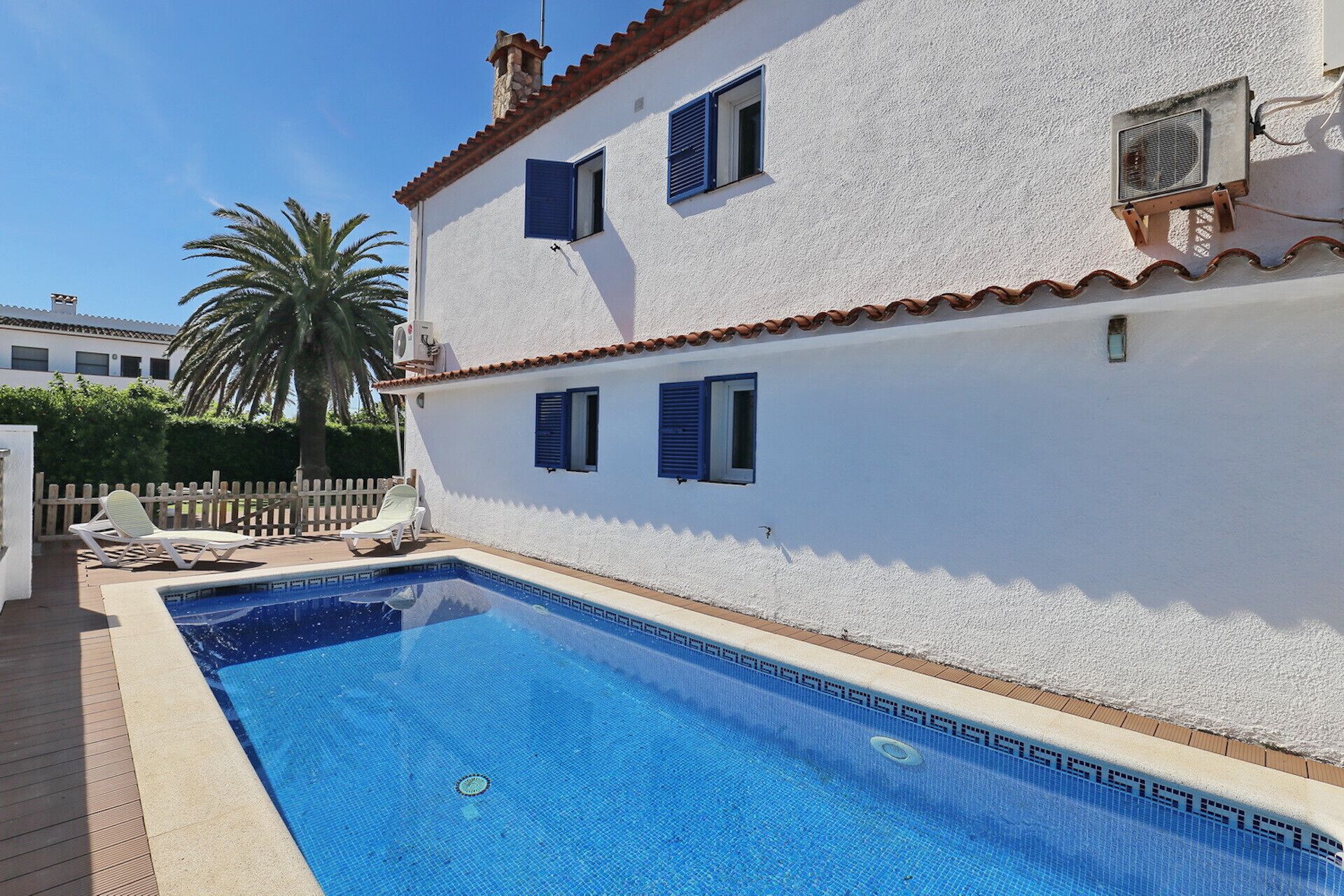 A two-story building with a swimming pool, white walls, and blue shutters.