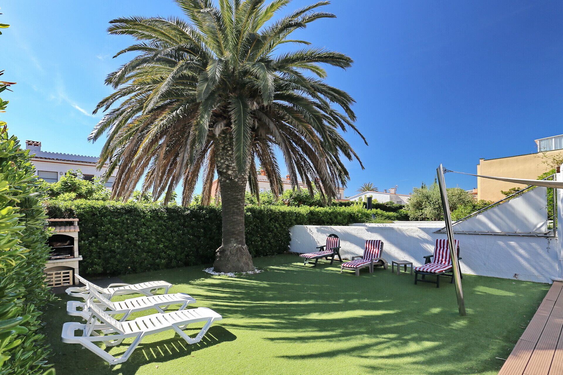 A backyard with artificial grass, a palm tree, and outdoor seating with striped cushions.