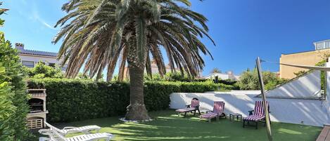 A backyard with artificial grass, a palm tree, and outdoor seating with striped cushions.
