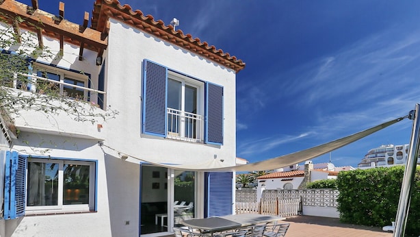 Une maison à deux étages avec un patio, une table entourée de chaises et un grand parasol.