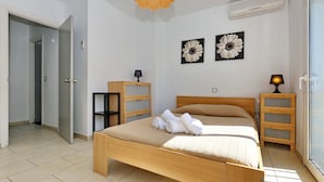 Une chambre à coucher avec un lit en bois, deux tables de chevet, une armoire et deux tableaux représentant des fleurs, accrochés au mur.