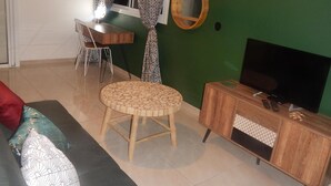 Una sala de estar con una pared verde, una mesa redonda de madera, un sofá, un mueble para la televisión y un reloj de pared.