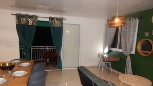 Un área de comedor con una mesa de madera dispuesta para dos personas, un sofá negro y una pequeña mesa redonda con una silla.