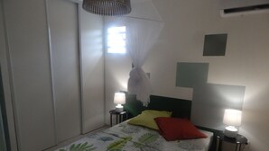 Un dormitorio con una cama, dos mesitas de noche, una lámpara auxiliar y una ventana con cortina blanca, además de un ventilador de techo.