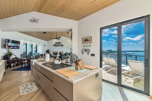 A modern kitchen with a central island, a dining area with chairs, and a large window overlooking a body of water.