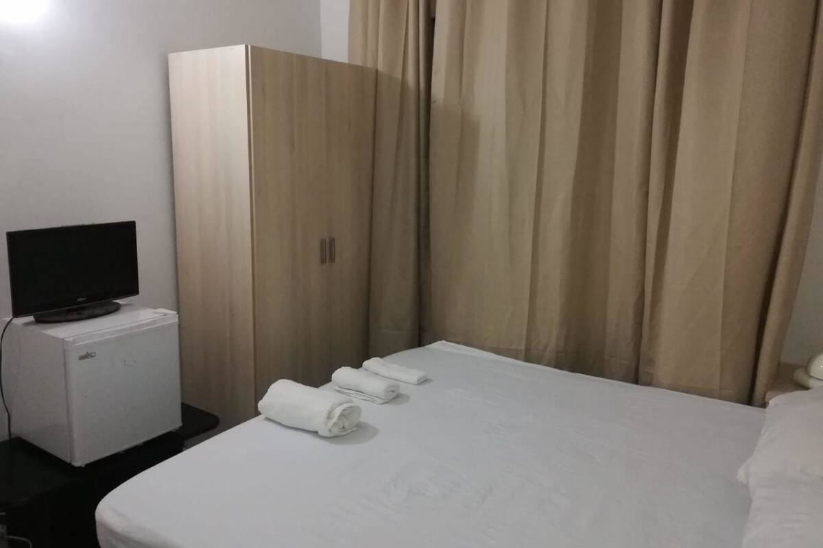 Una habitación de hotel con cama, televisión, refrigerador pequeño y armario.