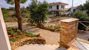 Un patio con muro de piedra, un árbol y una casa con tejado de tejas rojas.