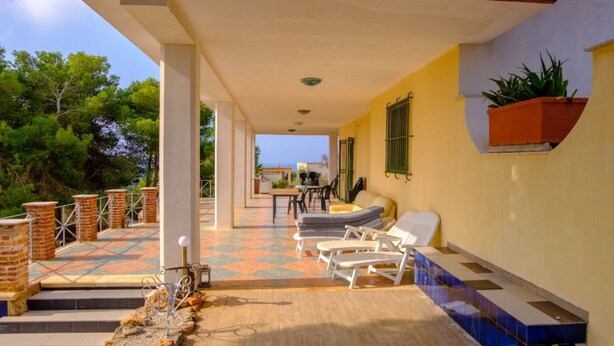 Un espacio al aire libre techado con terraza, asientos y vista al mar.