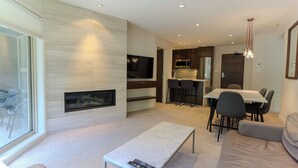 A modern living room with a fireplace, a dining area, and a kitchen. - Aspens #451 Renovated Ski-in Ski-out Location! Pool, Hot tubs, sleeps 4 (Whistler)