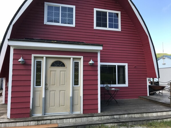 A red barn-style building with a beige front door, two windows, and a small patio area with a table and chairs.