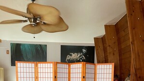 A room with a black leather chair, a small wooden table, a ceiling fan, and a traditional Japanese screen divider. - Furnished studio apartment (Unalaska)