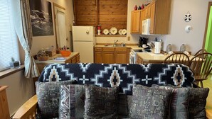 A cozy living area with a patterned sofa, wooden cabinets, and a kitchen in the background. - Furnished studio apartment (Unalaska)