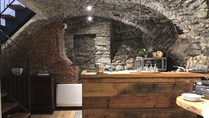 A rustic interior with exposed stone walls, a wooden counter, and a staircase leading to a loft area. - NicoMat Rooms (Domodossola)