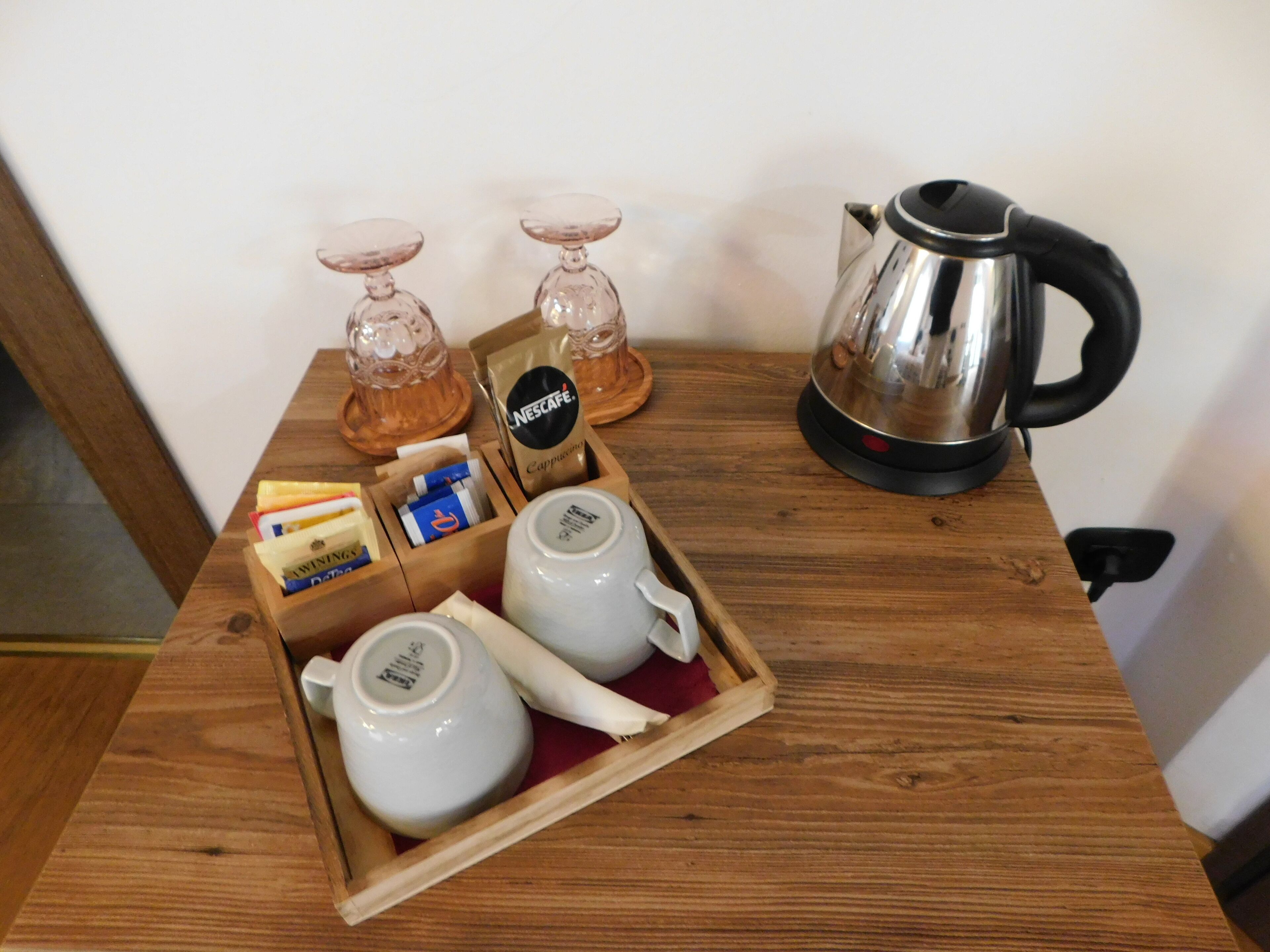 A wooden table with a tray containing two white teapots, a Nescafe coffee maker, and a box of tissues.