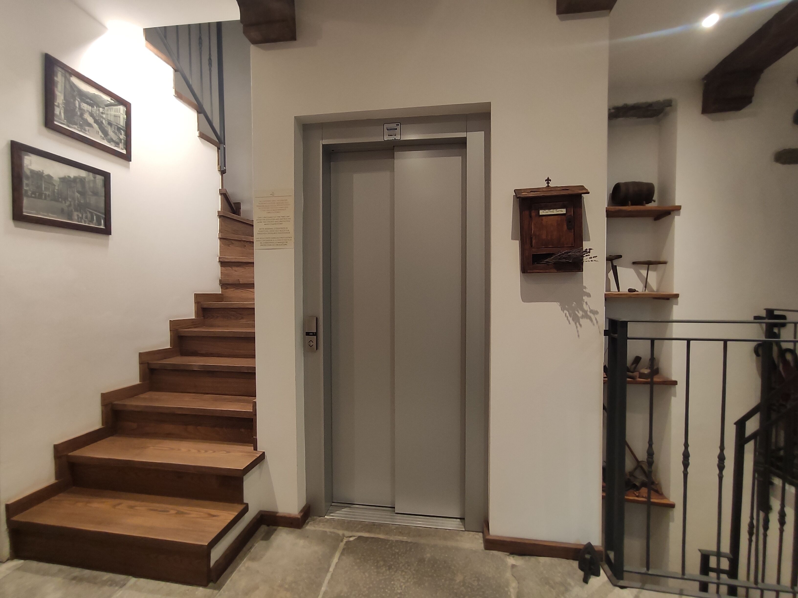 Una escalera que lleva a un ascensor, paredes de madera y un pequeño armario con herramientas.