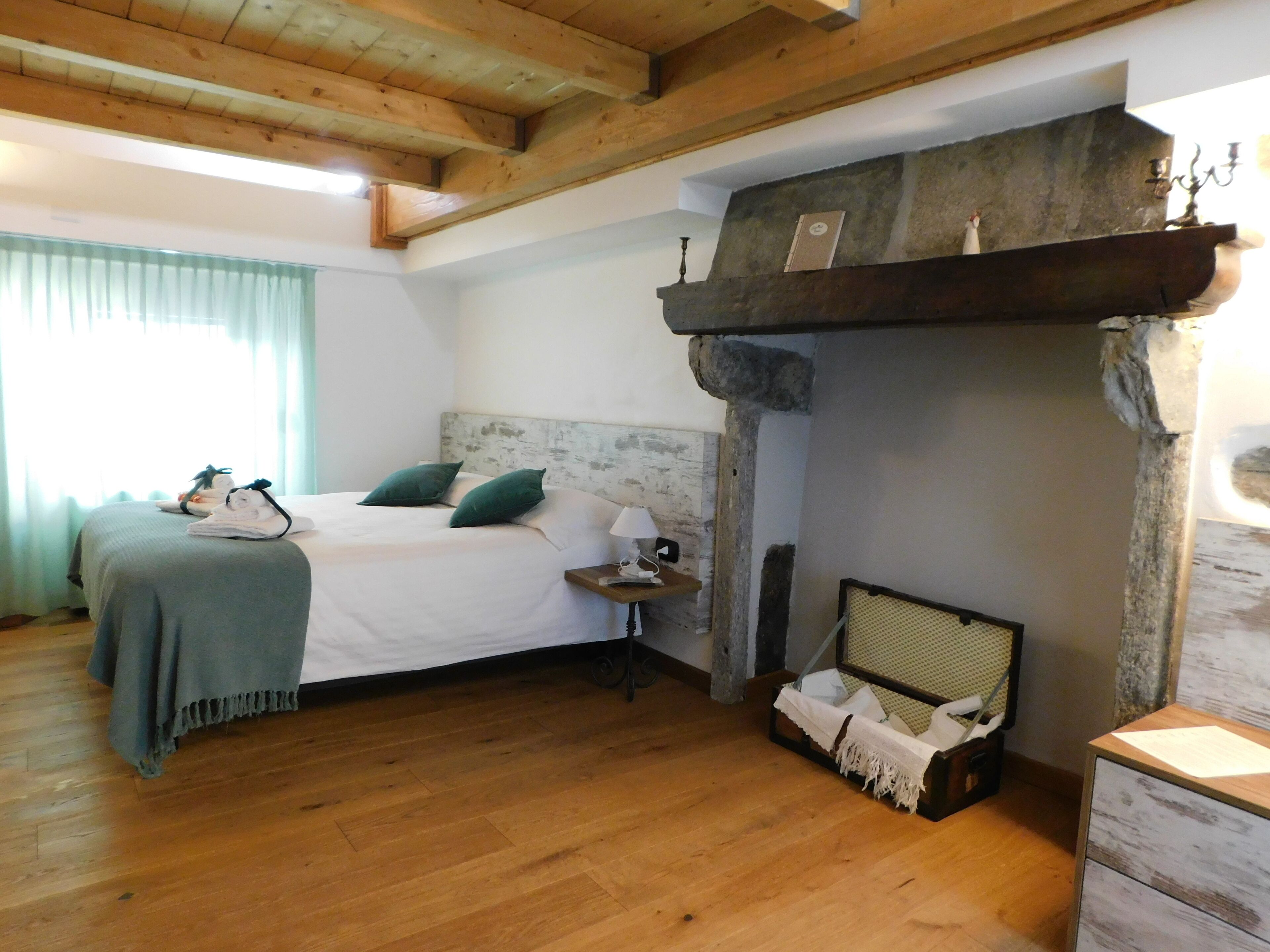 Un dormitorio con cama, mesita de noche, lámpara, una pequeña mesa, maleta y chimenea de piedra.