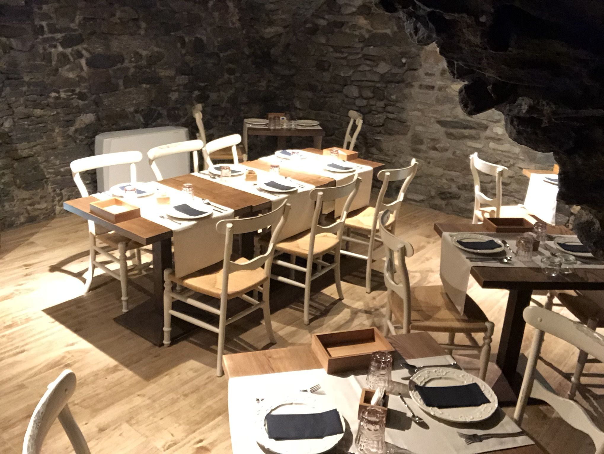 A rustic dining area with stone walls, wooden tables, and white chairs.
