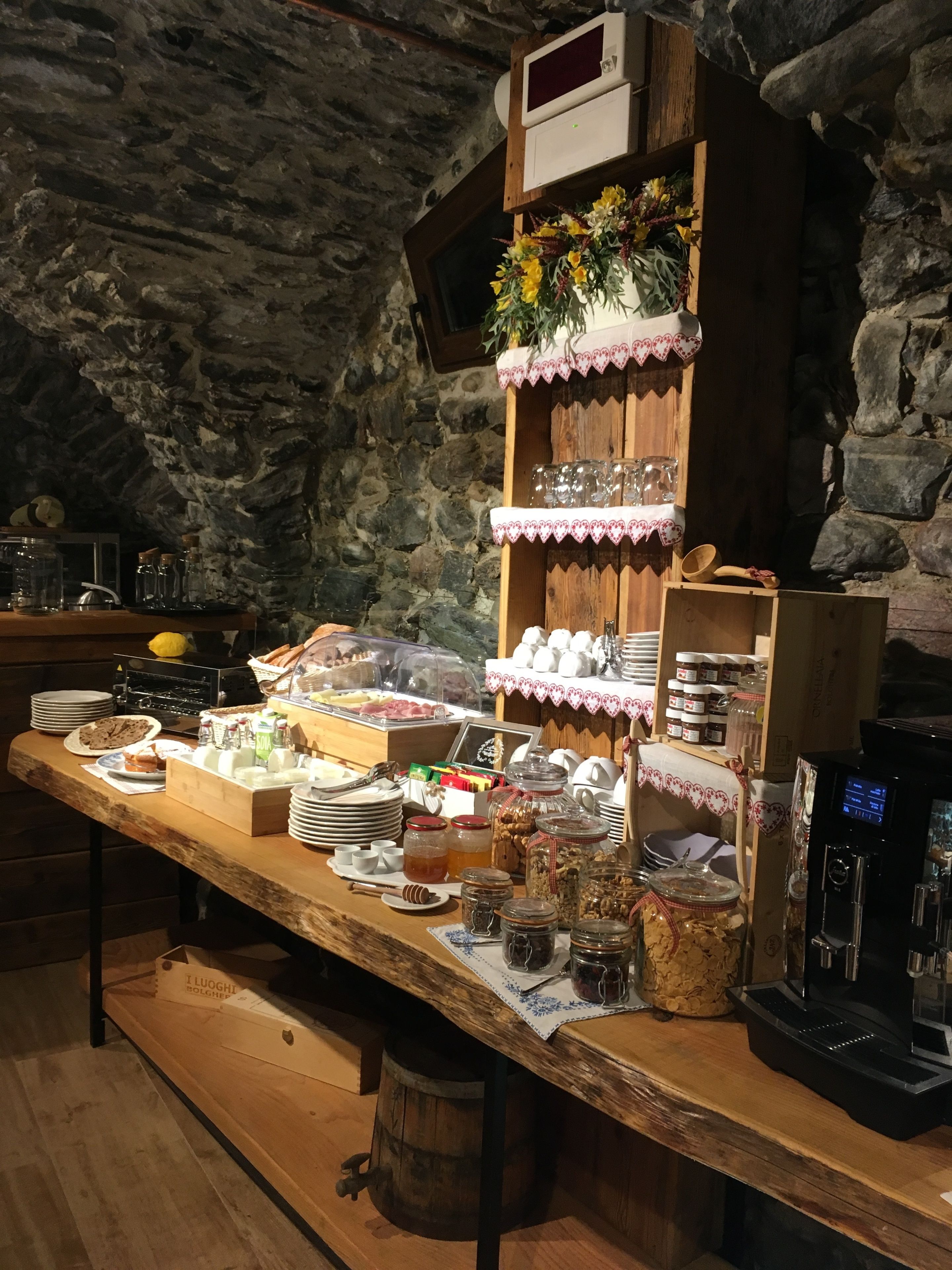 A breakfast buffet with various food items and condiments, set against a stone wall backdrop.