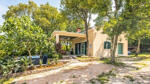 Uma casa moderna com um alpendre coberto, cercada por vegetação exuberante e um caminho de entrada de cascalho.