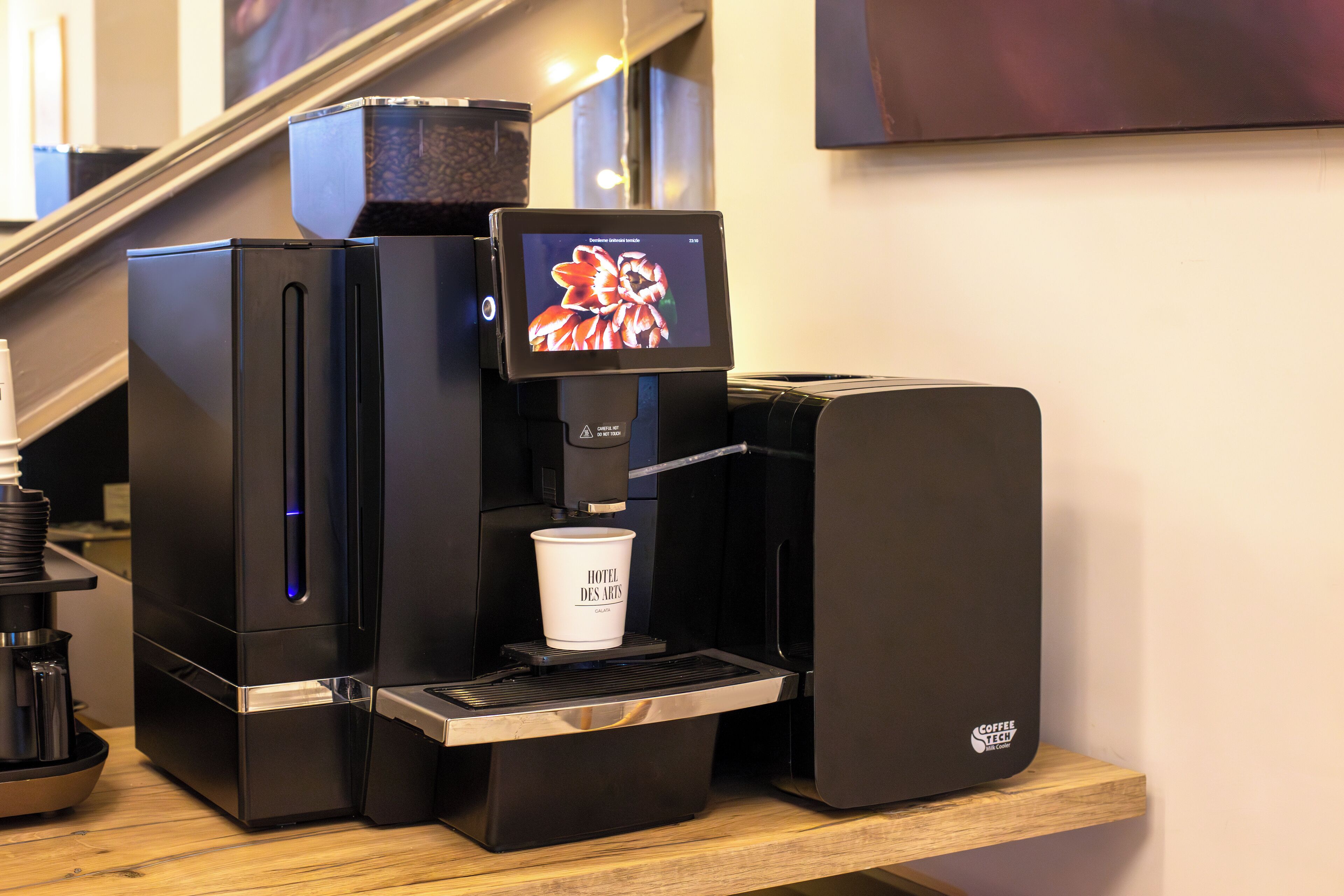 A coffee machine with a digital display and a cup holder, placed on a wooden counter.