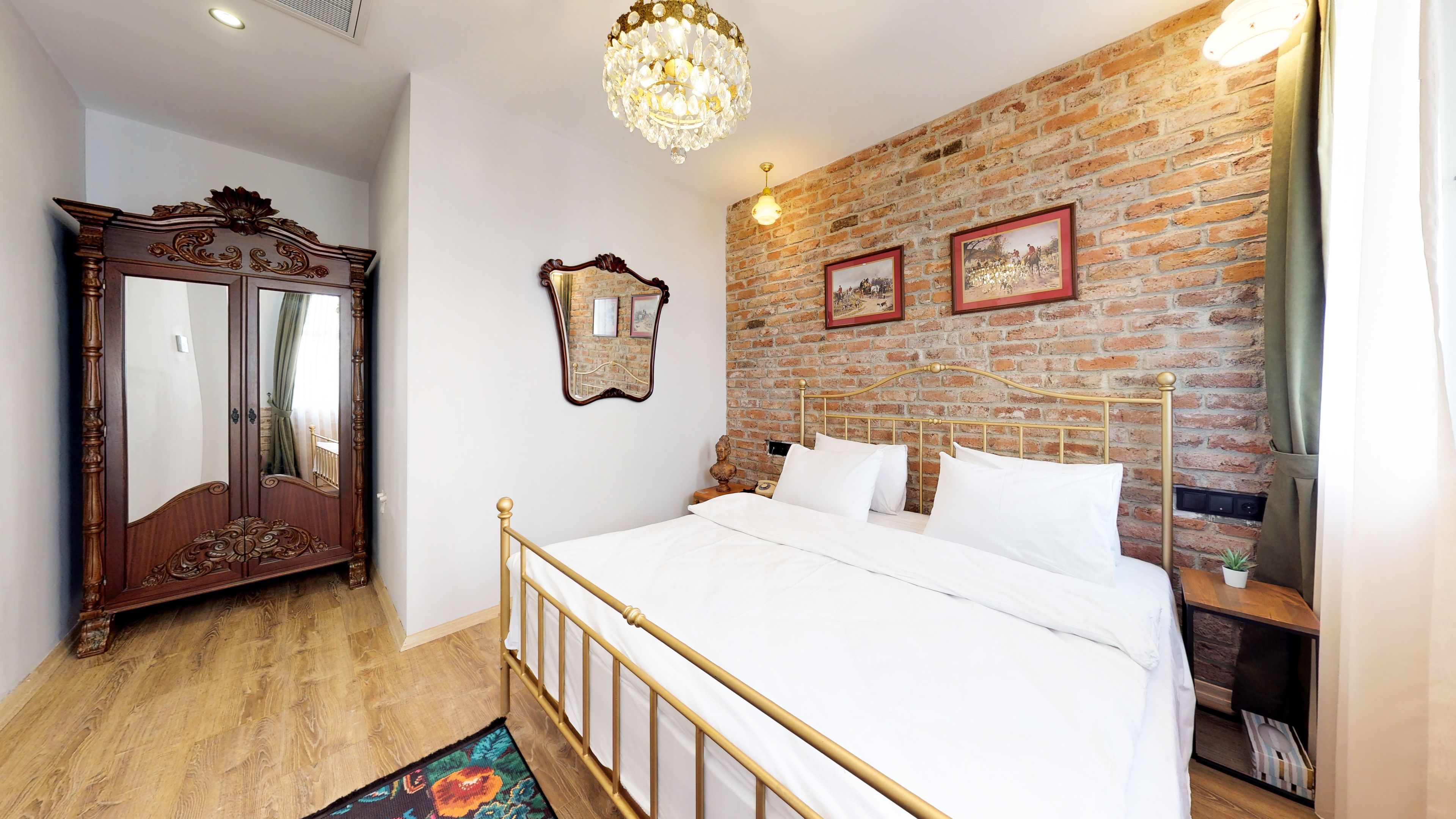 A bedroom with a brick wall, a large mirror, a chandelier, and a bed with white linens.