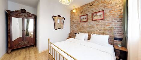 A bedroom with a brick wall, a large mirror, a chandelier, and a bed with white linens.