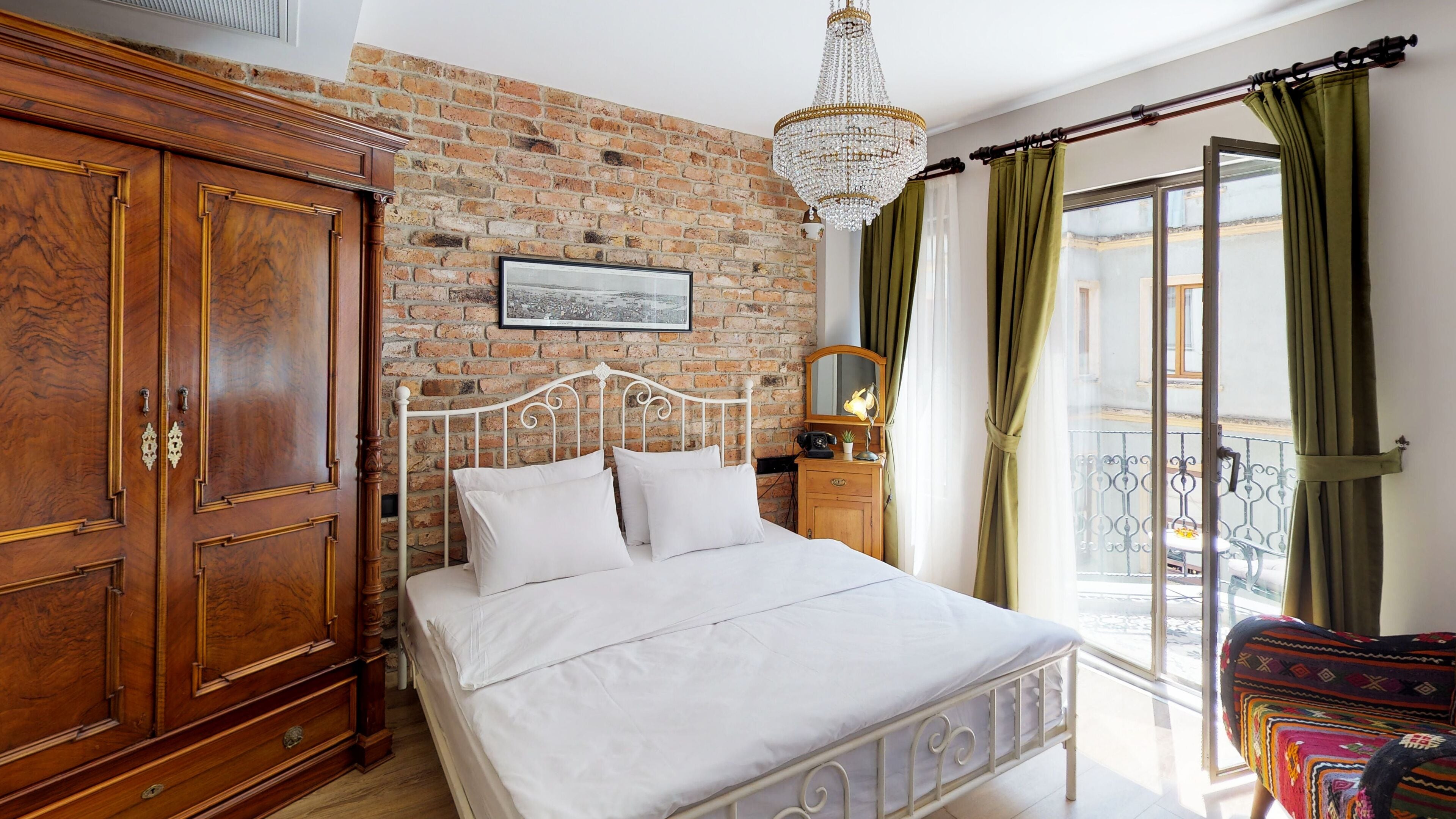 A bedroom with a brick wall, a large wooden wardrobe, a metal bed frame, and a balcony with green curtains.