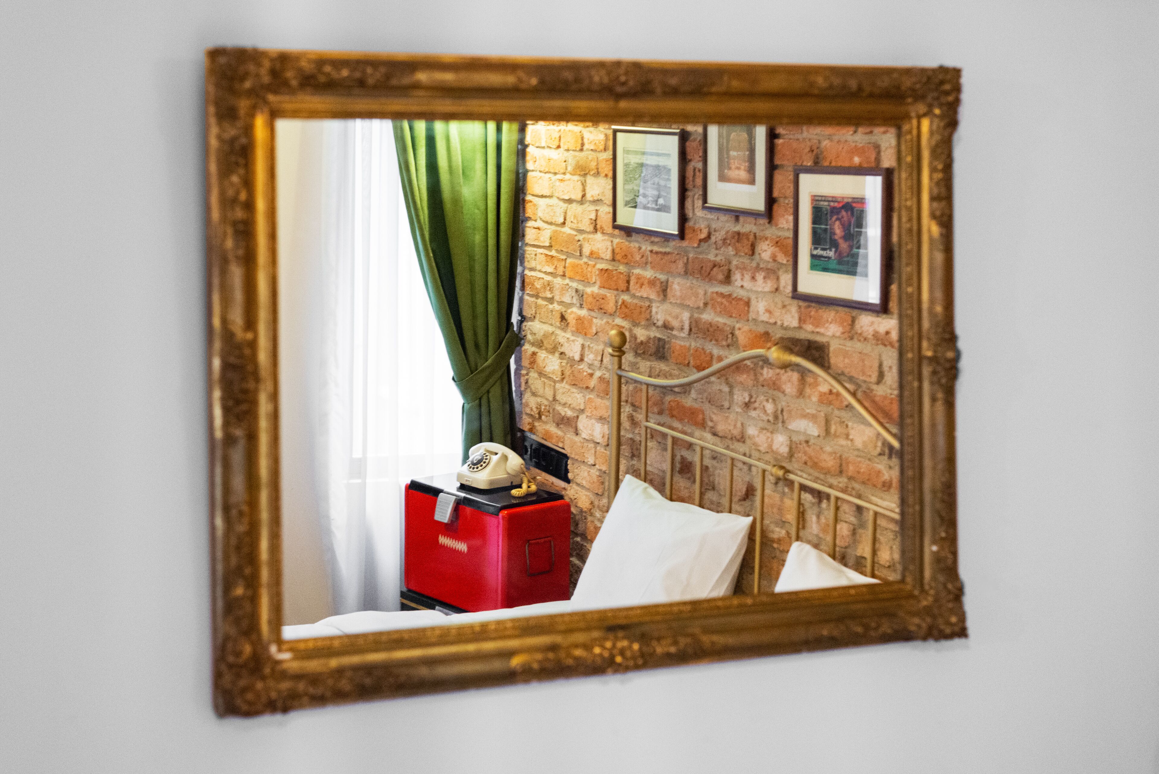 A room with a brick wall, a bed with white bedding, a red suitcase, and a vintage telephone.