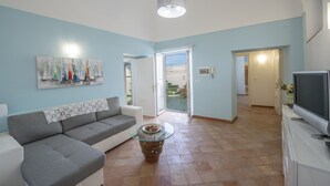 Una sala de estar con un sofá, una mesa de centro de cristal, un televisor y un cuadro en la pared.
