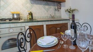 Una cocina con armarios de madera, salpicadero de azulejos y una mesa de comedor con platos, vasos y una botella de vino.