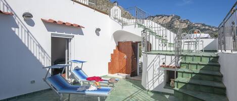 Una terraza en la azotea con sillones, una mesa de mimbre y una escalera que sube a un nivel superior.