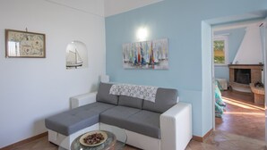 Una sala de estar con un sofá seccional gris, una mesa de centro de vidrio, una chimenea y un cuadro de veleros en la pared.