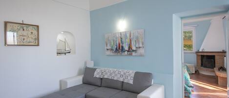 Ein Wohnzimmer mit einem grauen Ecksofa, einem Glastisch, einem Kamin und einem Segelbootbild an der Wand.