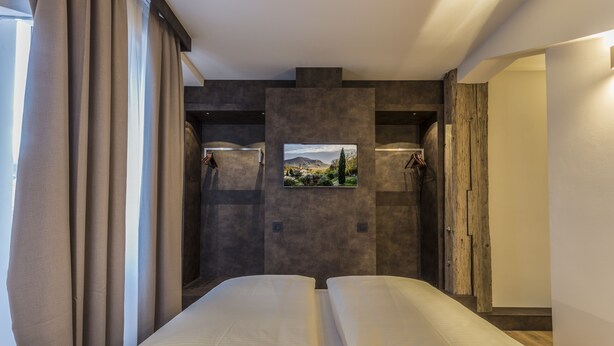 A modern hotel room with a large bed, a mounted TV, and a view of a mountainous landscape. - Hotel Jakobslust (Gruenstadt)