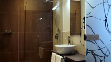 Un baño moderno con ducha envuelta en vidrio, un espejo grande y un lavabo blanco.