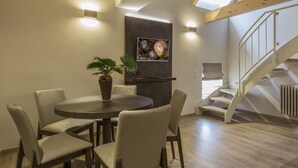 A dining area with a round table and chairs, a potted plant, and a wall-mounted TV. - Hotel Jakobslust (Gruenstadt)