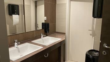 A bathroom with two sinks, a mirror, a soap dispenser, and a trash bin.