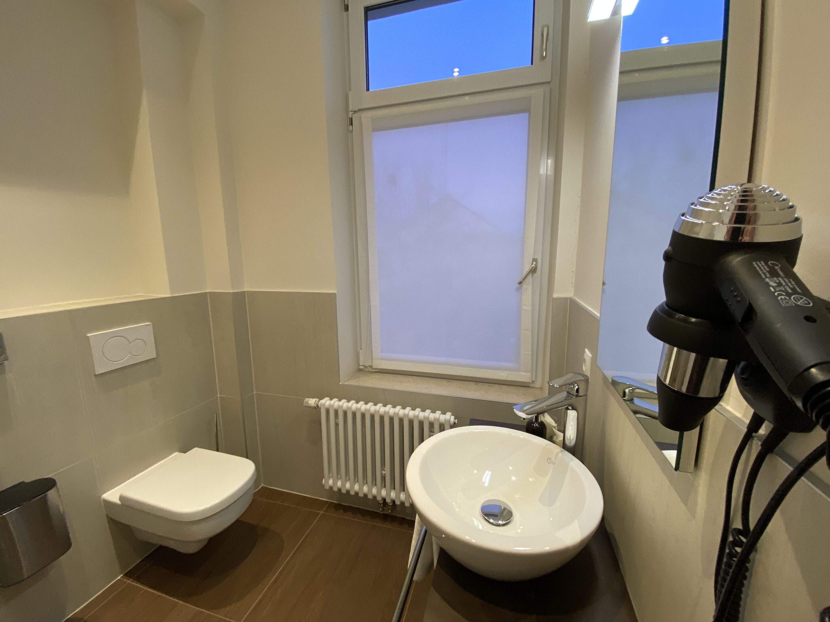 A small bathroom with a toilet, sink, and a hairdryer on the wall.