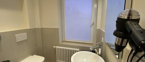 A small bathroom with a toilet, sink, and a hairdryer on the wall.