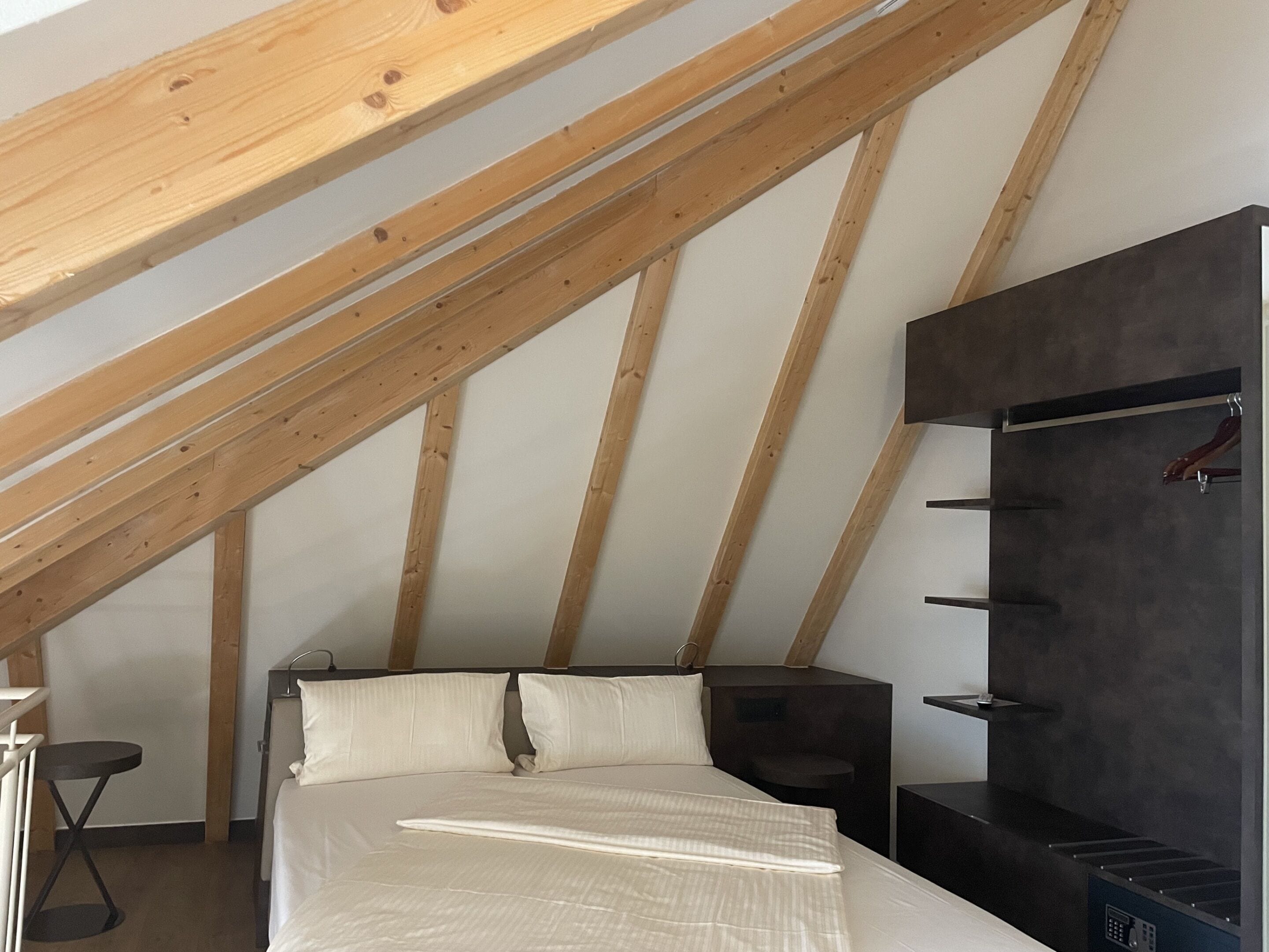 Un dormitorio con techo inclinado, cama, armario y una mesita.