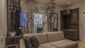 A modern living room with a sofa, a glass partition with tree silhouettes, and a built-in shelving unit. - Hotel Jakobslust (Gruenstadt)