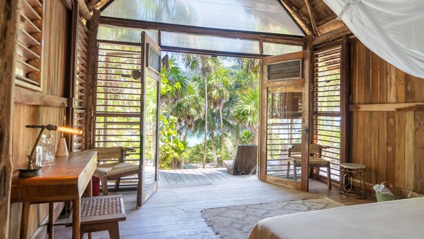 A wooden room with a large glass door leading to a deck with a view of palm trees. - Rancho Sarah Tulum in Sian Ka’an  (Tulum)