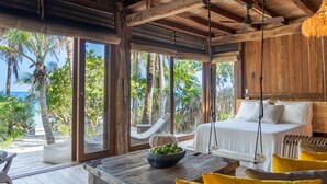A wooden room with a bed, a table with a bowl of fruit, and a view of the beach and palm trees. - Rancho Sarah Tulum in Sian Ka’an  (Tulum)